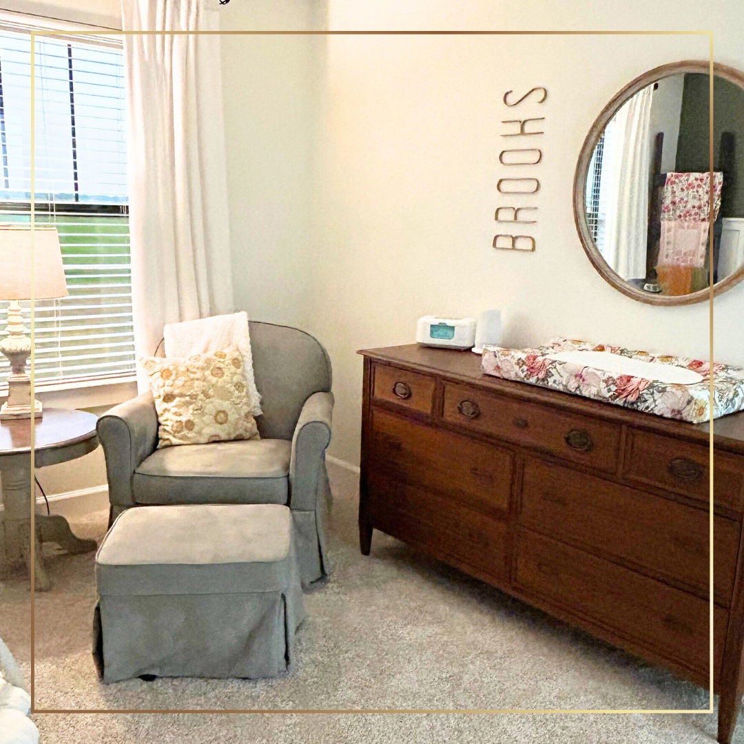 a baby's room with a chair, dresser and mirror