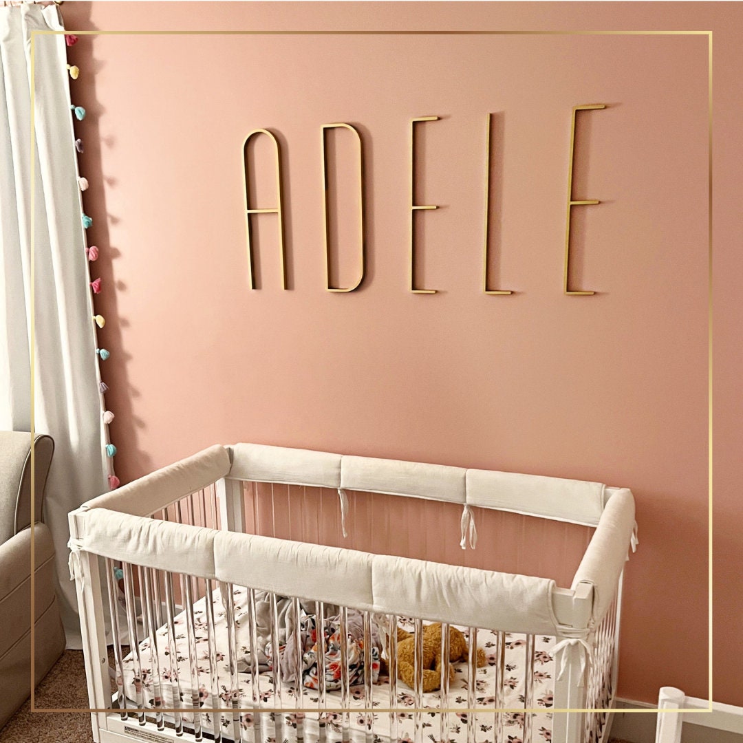 a white crib in a pink room with a name on the wall