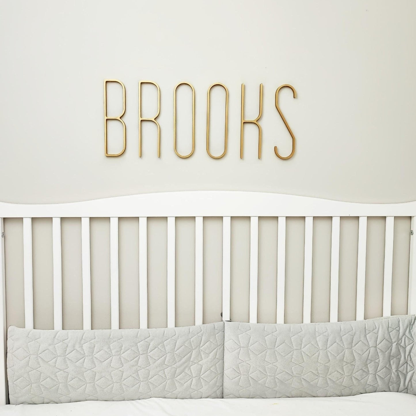 Gold modern skinny name BROOKS above baby crib on a nursery wall
