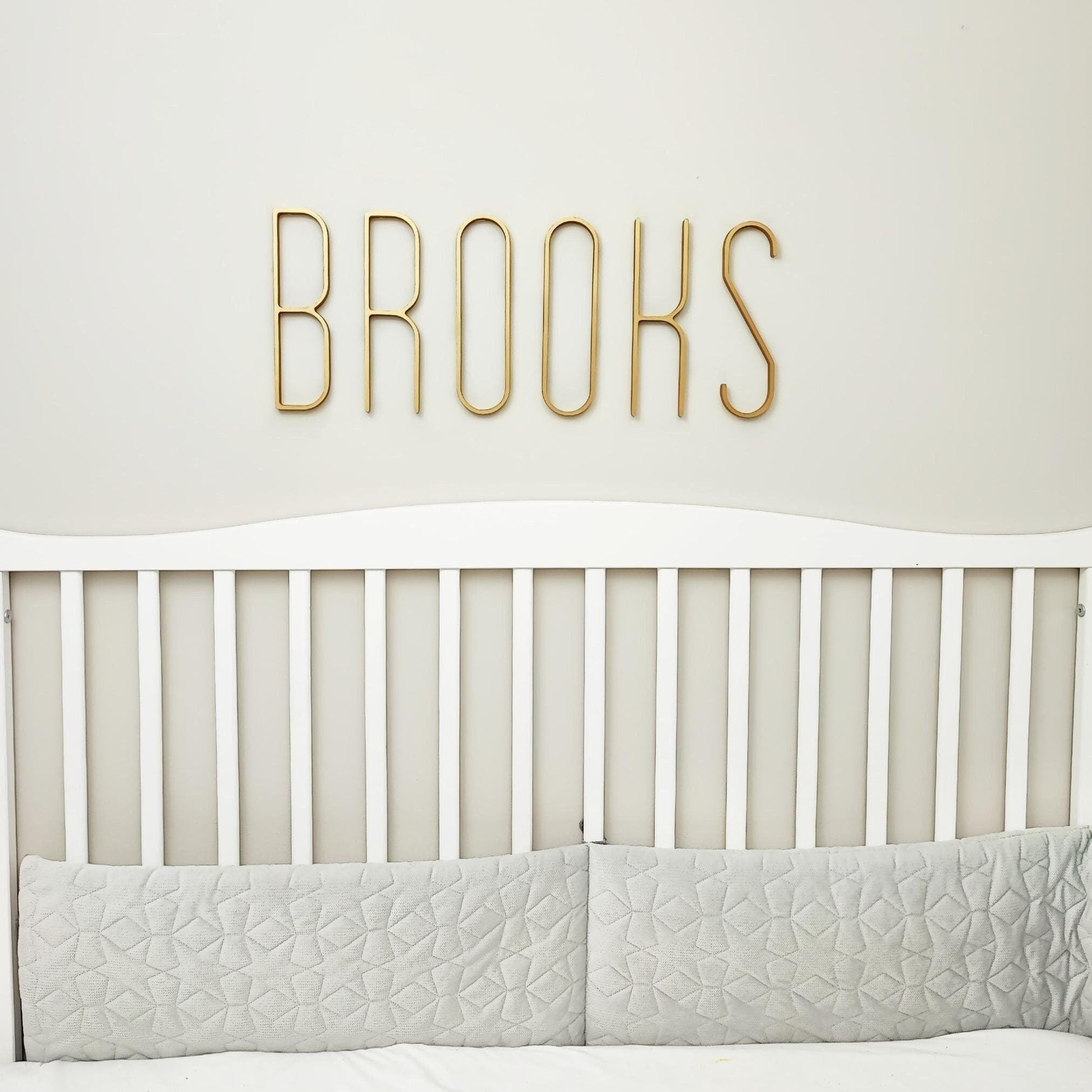 Gold modern skinny name BROOKS above baby crib on a nursery wall