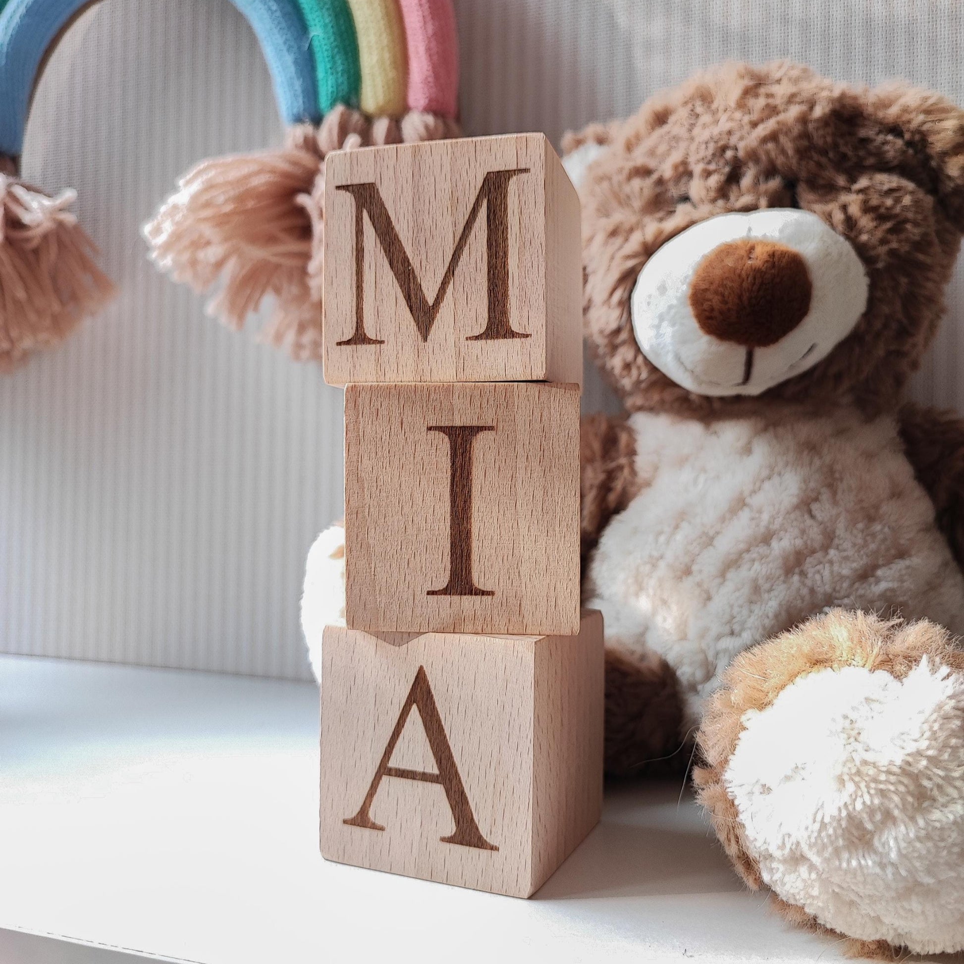 MIA name engraved on natural wooden blocks, standing on a white nursery shelf next to boho baby decorations