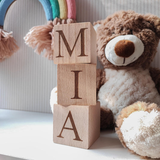 MIA name engraved on natural wooden blocks, standing on a white nursery shelf next to boho baby decorations