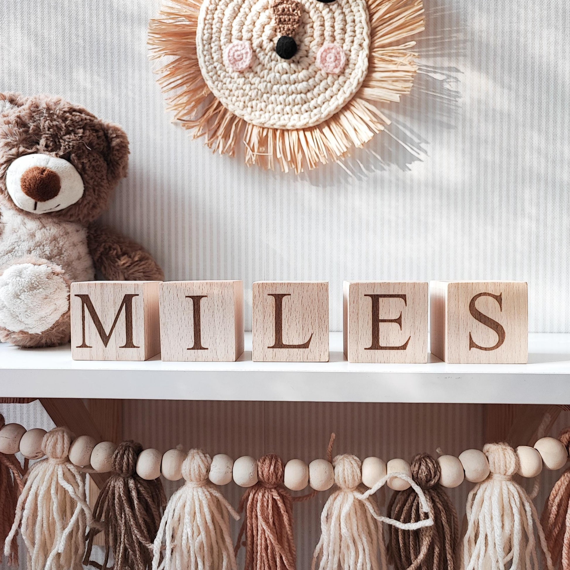 MILES name engraved on natural wooden blocks, standing on a white nursery shelf next to boho baby decorations