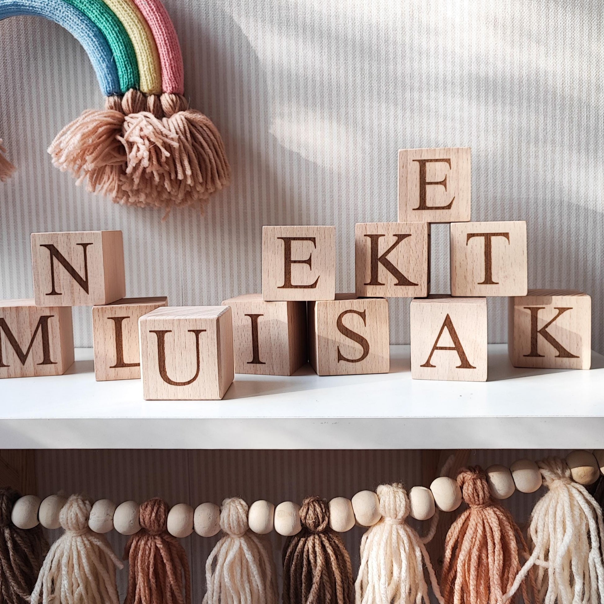 letters of the alphabet engraved on natural wooden blocks, standing on a white nursery shelf next to boho baby decoration