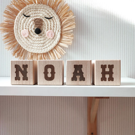 western style letters NOAH on wooden name blocks standing on a white shelf next to neutral nursery decor